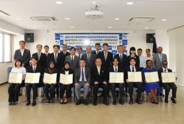 学長、研究科長、役員、指導教員、修了生と記念撮影。修了生は学位記をひろげて和やかな雰囲気。
